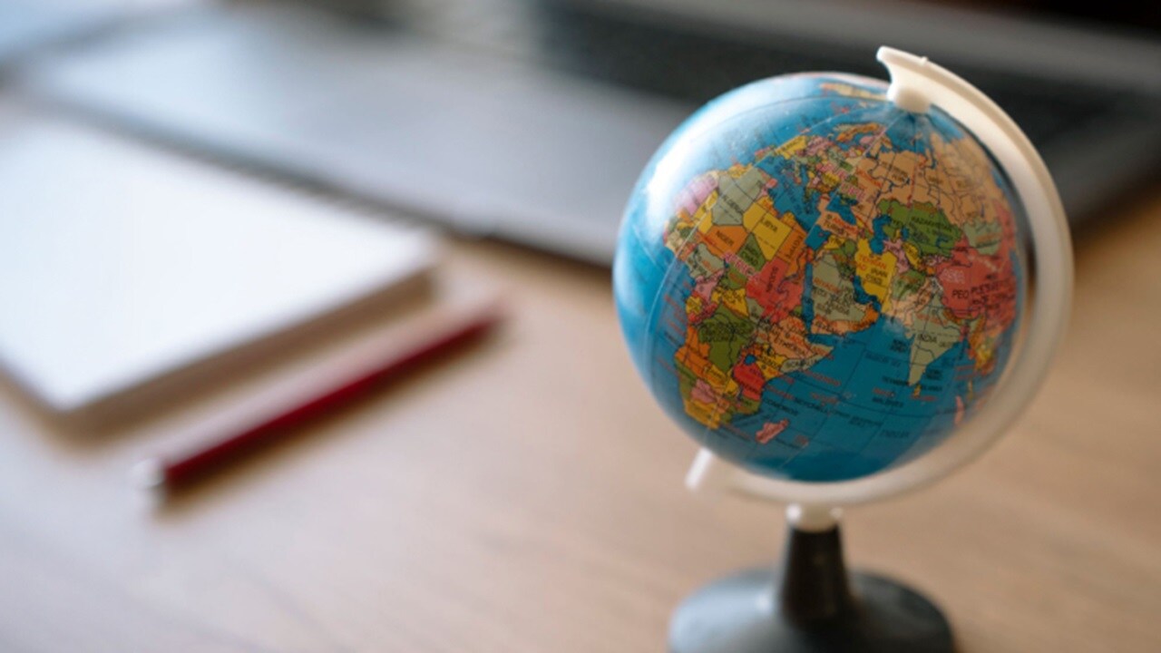 A globe sits on a desk with a laptop visible in the background, suggesting a study or work environment.