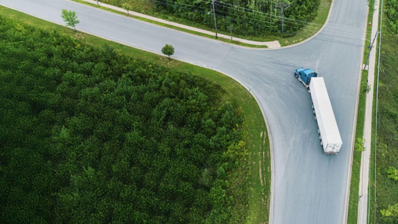 Aerial view of a truck driving along a winding road surrounded by greenery and fields.