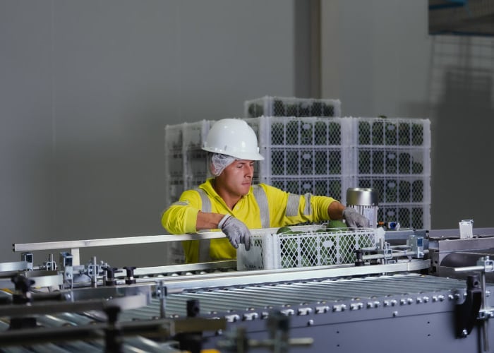 A worker in a yellow safety vest operates a machine in a factory setting, focusing on their task.