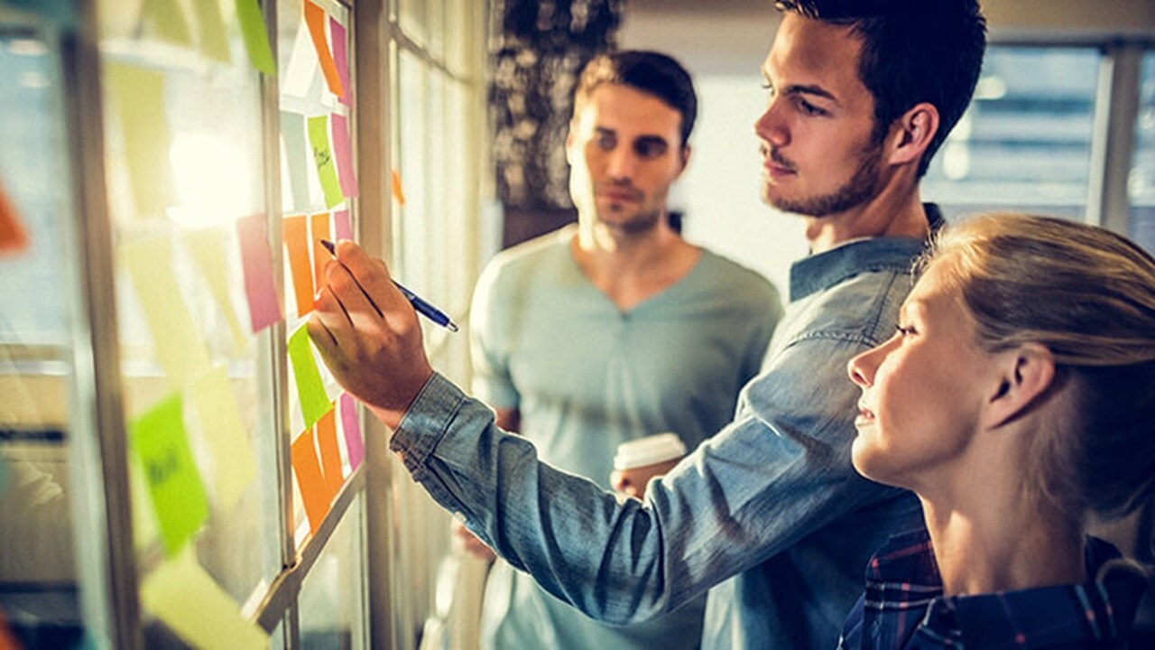 Three Maersk employees in an office with one of them writing on a sticky note.