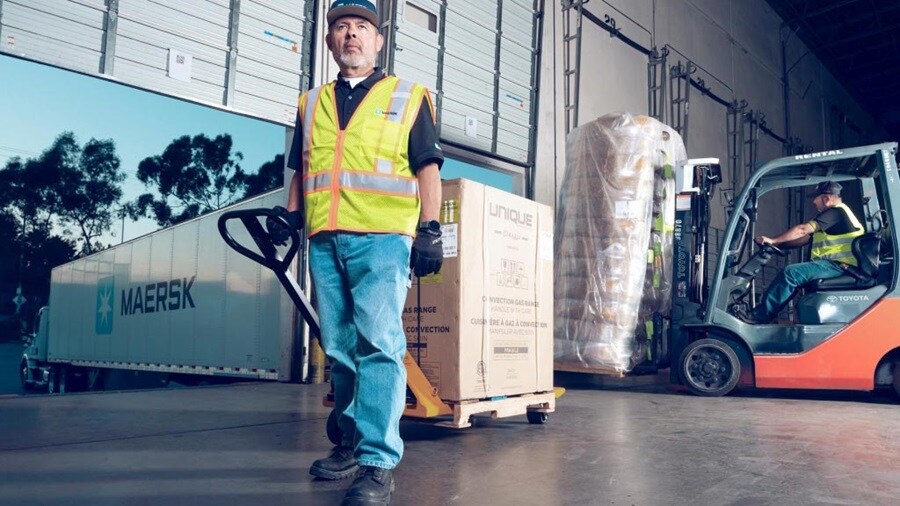  A man wearing a safety vest operates a forklift truck in a warehouse setting.