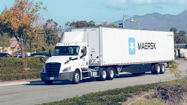 A white truck traveling down a rural road with trees lining the sides.