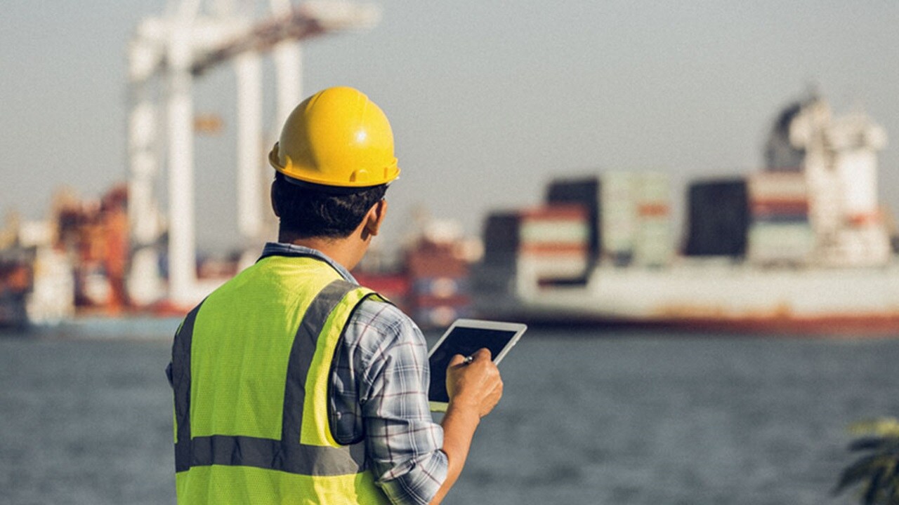 A man in a hardhat with an iPad at port
