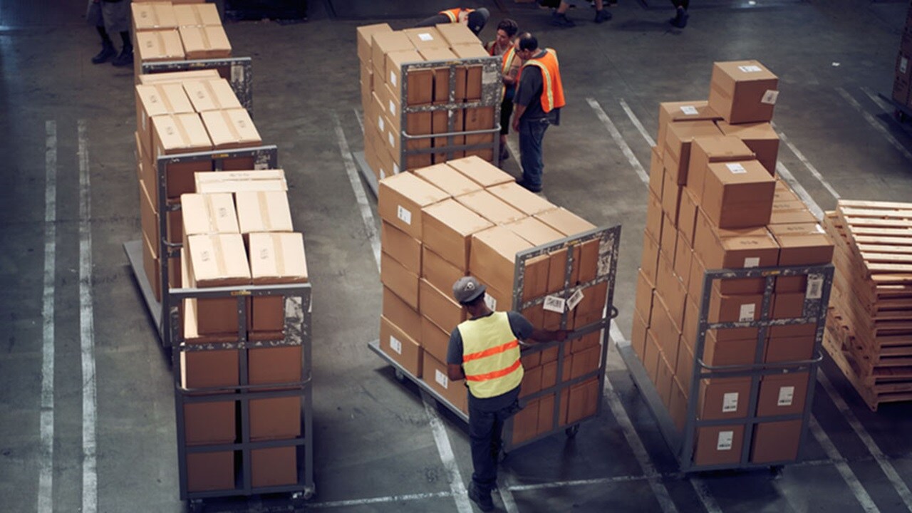 Three warehouse workers push trolleys of packages to illustrate the benefits of integrated logistics