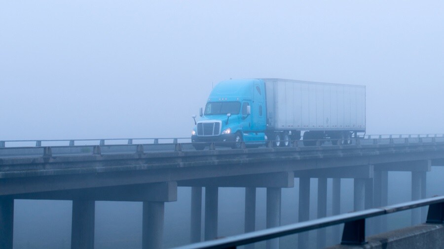 Blue truck driving on a foggy bridge