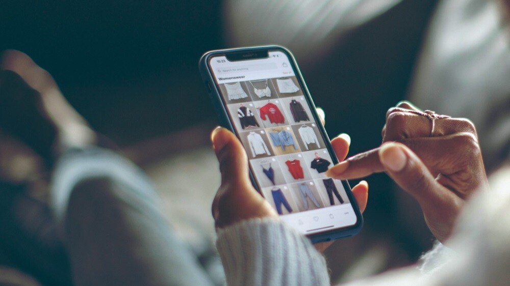 A person holding a mobile phone with apparel tiles on the screen.