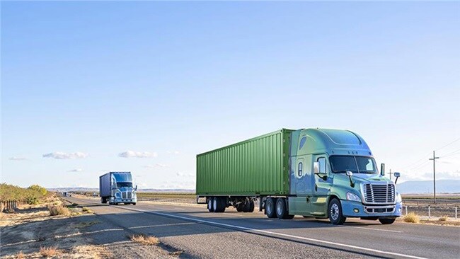 Two large trucks traveling down a highway.
