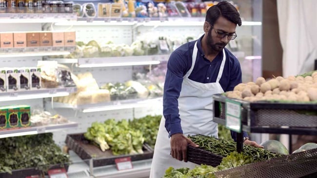 employee with white apron and blue shirt organizing products at the store
