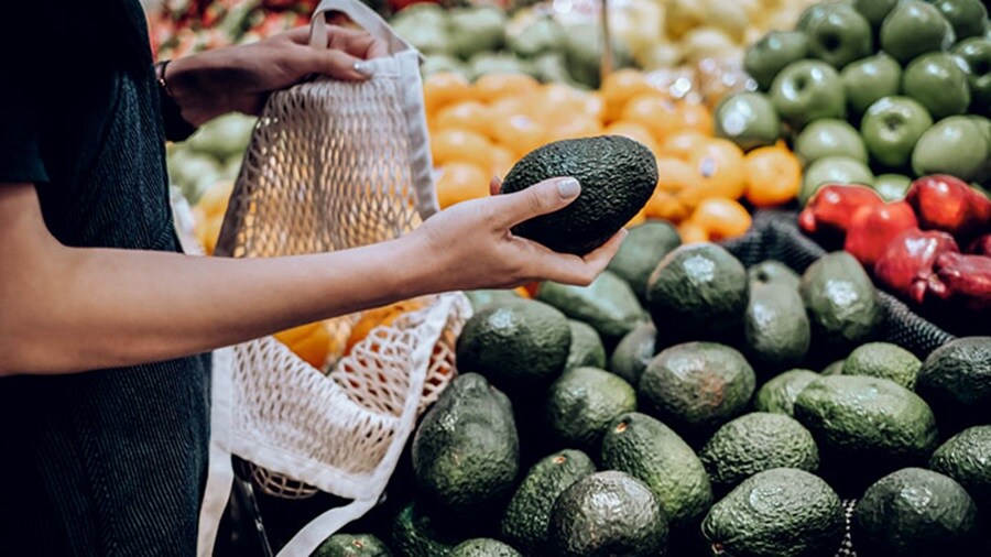 Hand of a woman taking an avocado out of a shelf