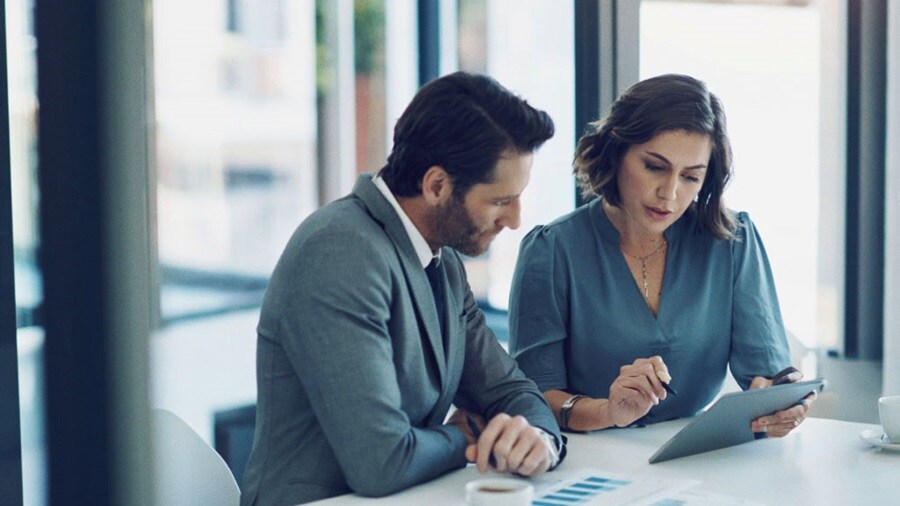 Two professionals reviewing data on a tablet in a modern office setting.