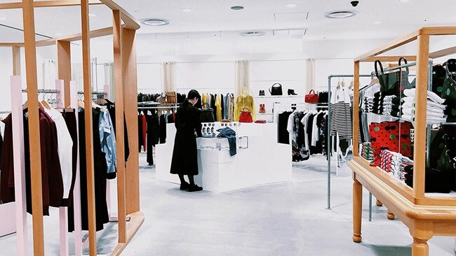 A woman browsing through clothes in a retail store, examining various garments on display.