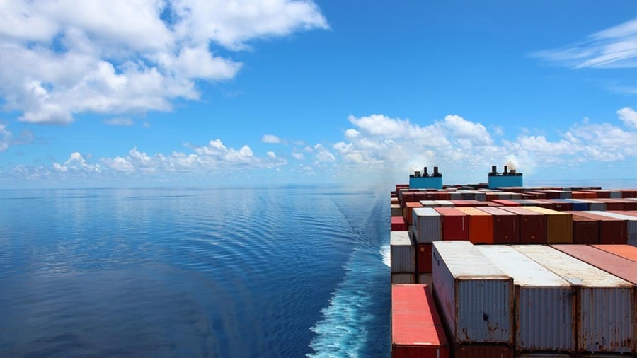 A container ship glides through a clear blue ocean, representing decarbonisation in shipping. 
