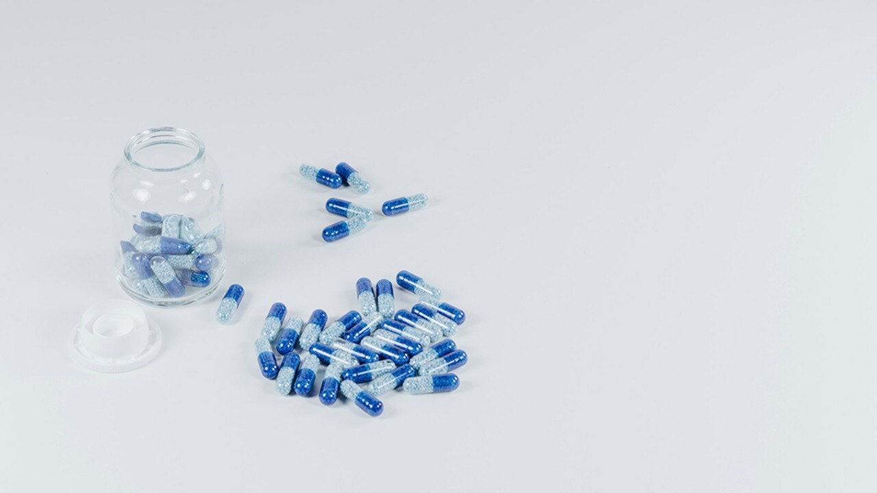 White and gray pills beside jar