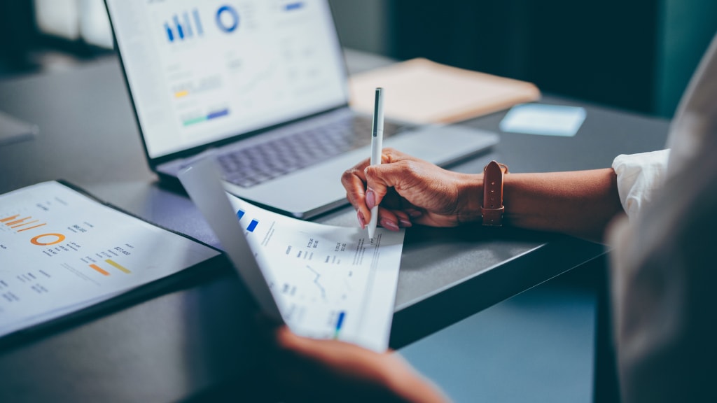 Close-up of a workstation with a hand holding a pen and looking at data