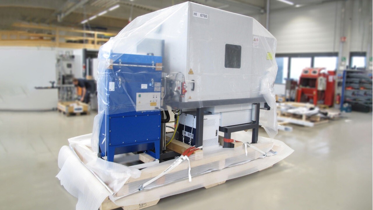 A machine covered in plastic is stored in a warehouse, indicating it is protected for transport or storage.