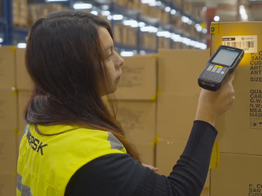 A warehouse worker scans a shipping label on a large cardboard box with a handheld device.
