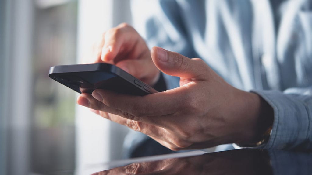 A person holding a cell phone in their hand, looking at the screen with a focused expression.