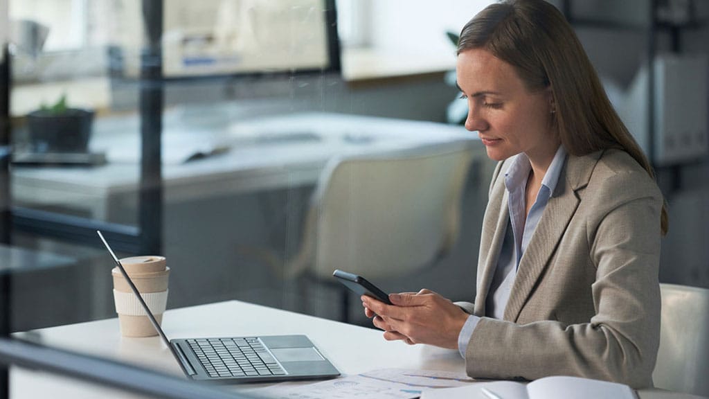 A professional woman in a business suit is using her smartphone, appearing focused and engaged.