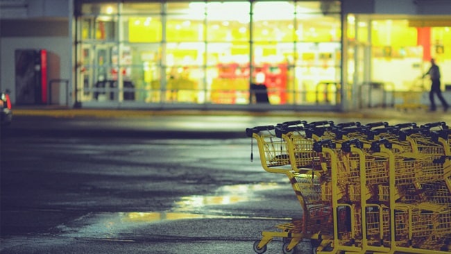 A series of yellow trolleys with a supermarket in the background.