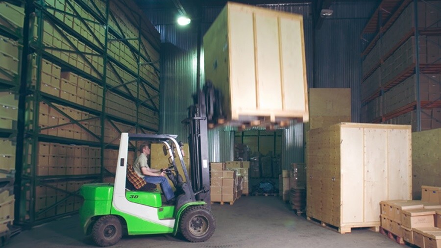 Male organizing boxes in a warehouse using a forklift 