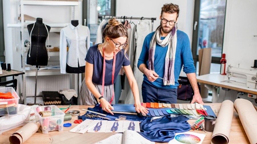 A female and a male tailor measuring dimensions.