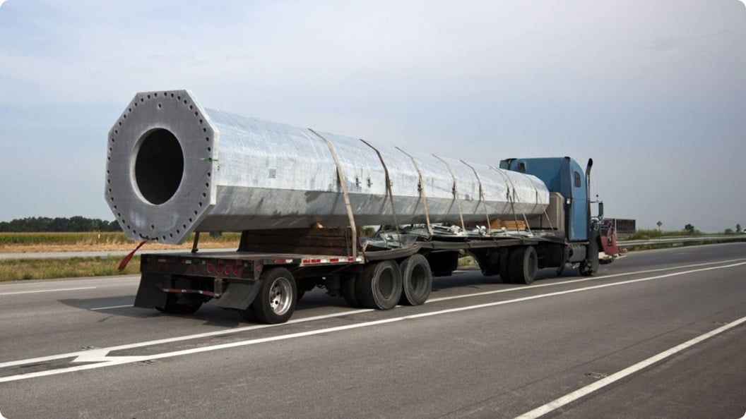 A large pipe is being transported on a flatbed truck down a highway.