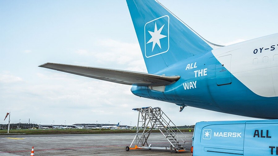 Maersk aircraft tail with 'All the Way' slogan and a Maersk van on the tarmac at an airport.