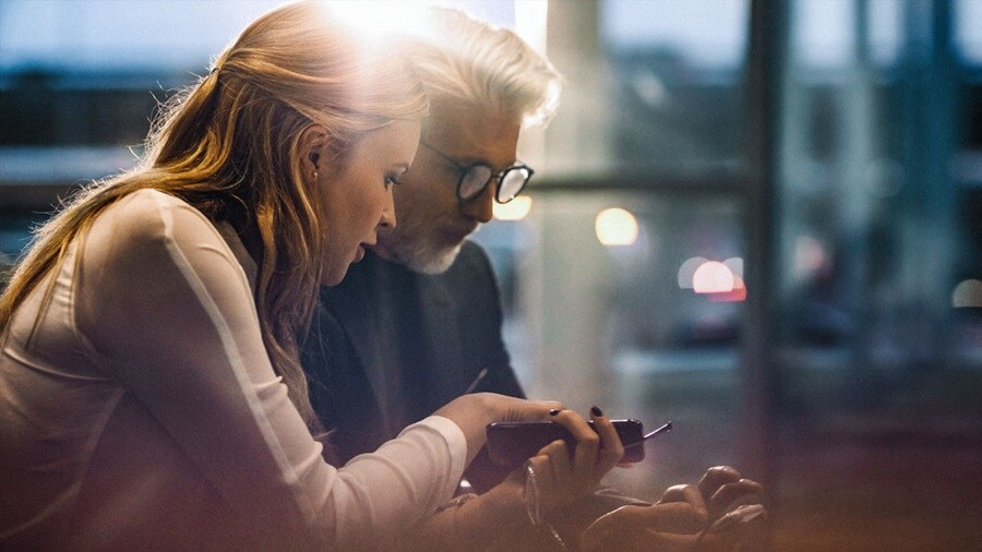 A businessman sits next to a woman who is scrolling through her phone.