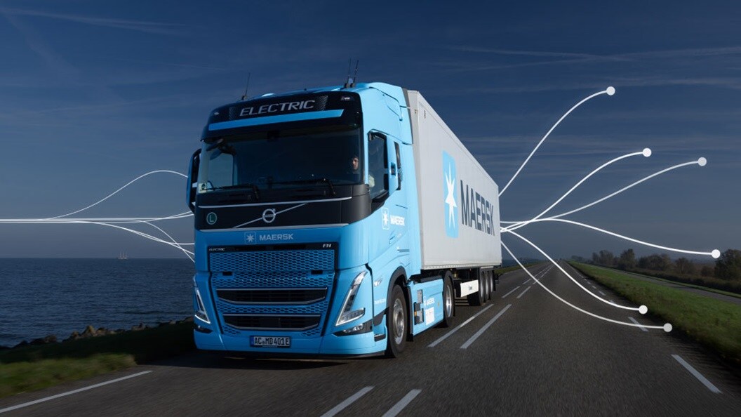 A maersk truck drives along a road under a clear blue sky, showcasing a serene outdoor scene.