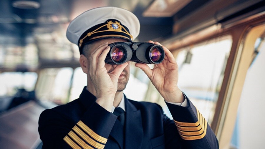 Ship captain in uniform looking through binoculars.