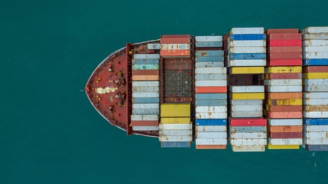 Aerial view of a large container ship loaded with numerous colorful shipping containers on the open sea.