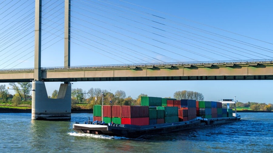 Cargo barge carrying shipping containers under a bridge.