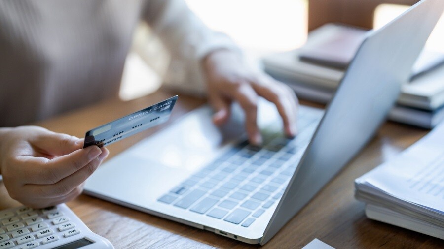 Person holding a credit card while using a laptop for online payment.