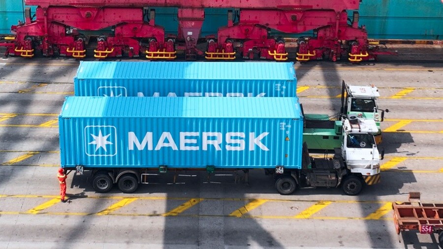 Two trucks transporting blue Maersk shipping containers at a port.