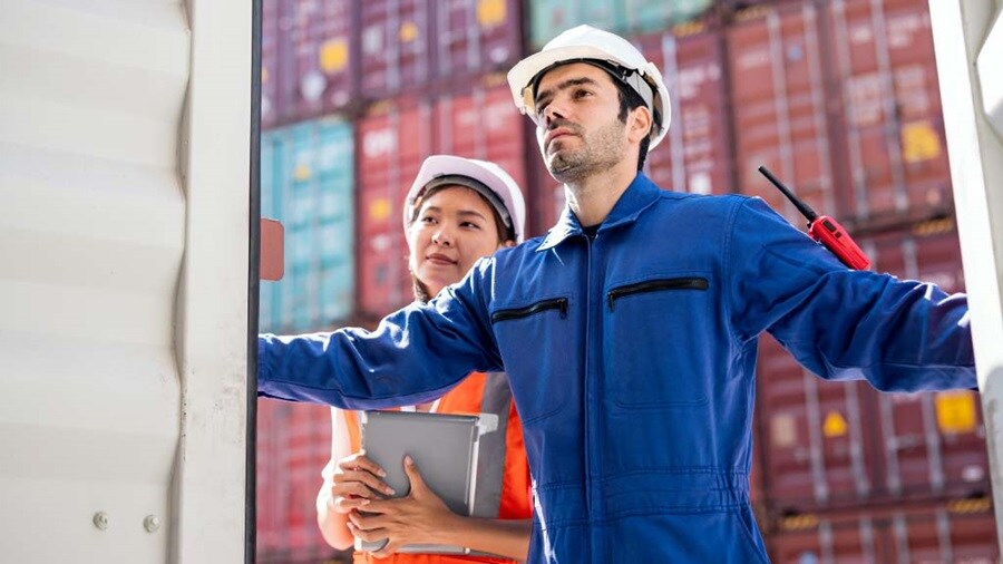 Two workers inspecting a shipping container, surrounded by stacked cargo units.