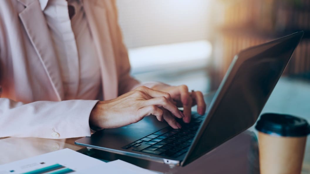 Business professional typing on laptop with coffee cup on desk