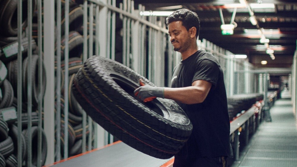 A man holds a tire in a spacious warehouse filled with shelves and equipment.