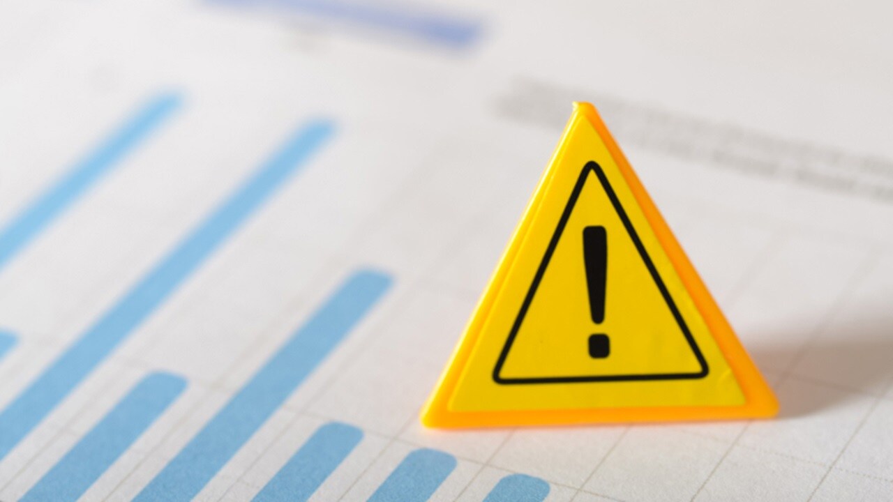 Yellow warning triangle sign placed on financial chart indicating supply chain risk signals