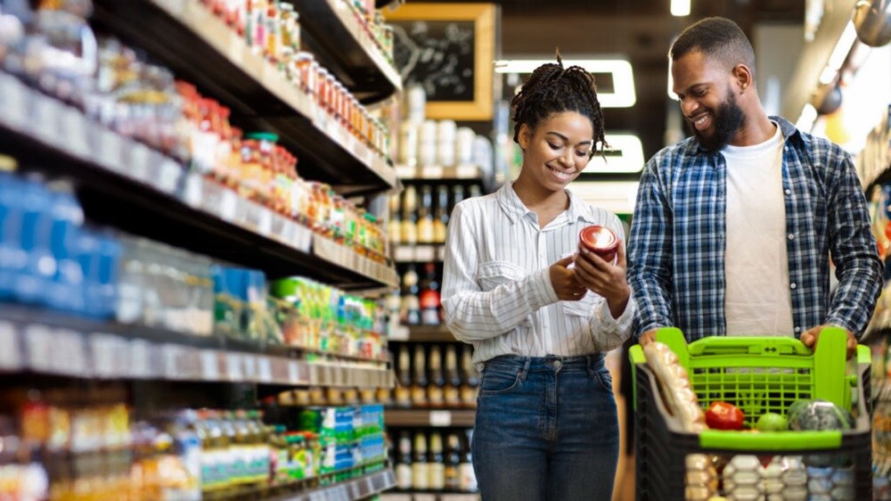 A man and woman reviewing packaged goods on supermarket shelves.