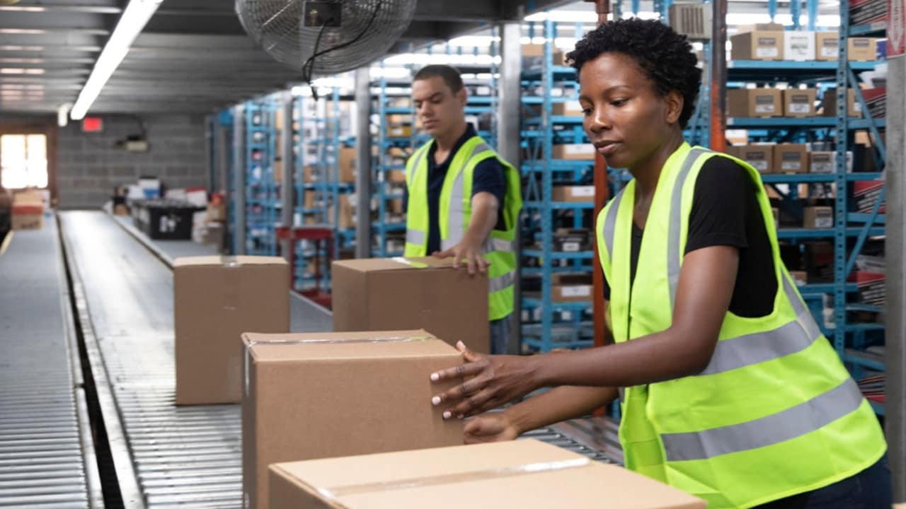 Warehouse workers in safety vests sorting packages on a conveyor belt for distribution
