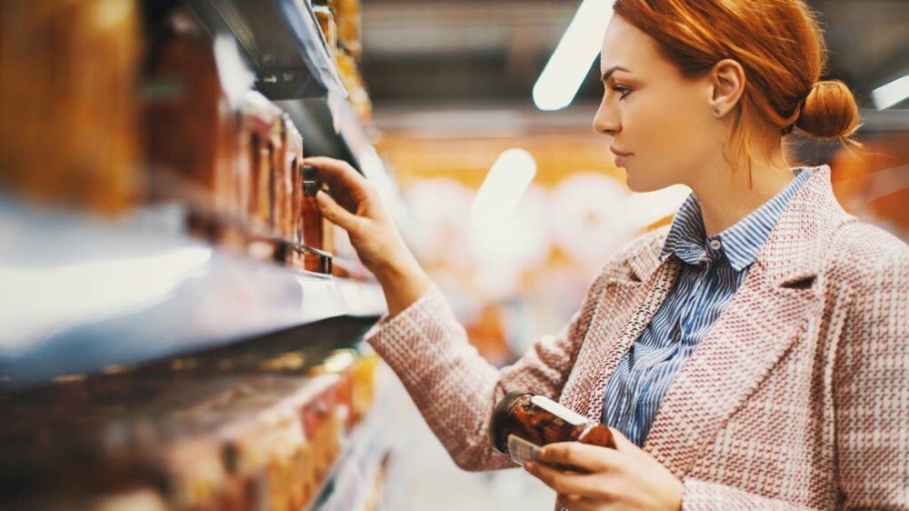 A woman examining a shelf filled with various food items in a grocery store.