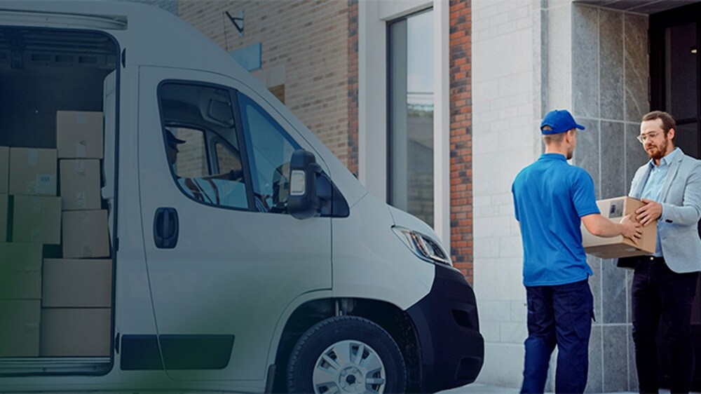 E-commerce last-mile delivery – A delivery man handing a package to a customer with a truck containing packages behind him.