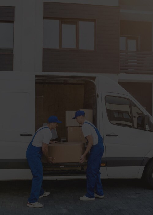 Two logistics workers unloading boxes from a delivery van in front of a modern residential building, representing efficient last-mile delivery services.