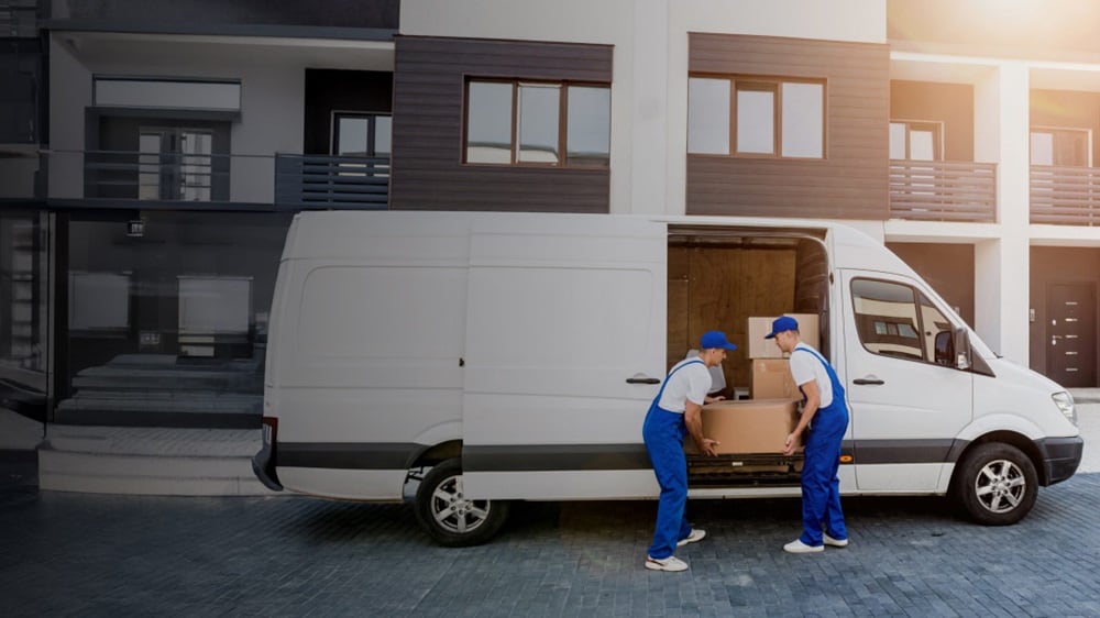 Two logistics workers unloading boxes from a delivery van in front of a modern residential building, representing efficient last-mile delivery services.