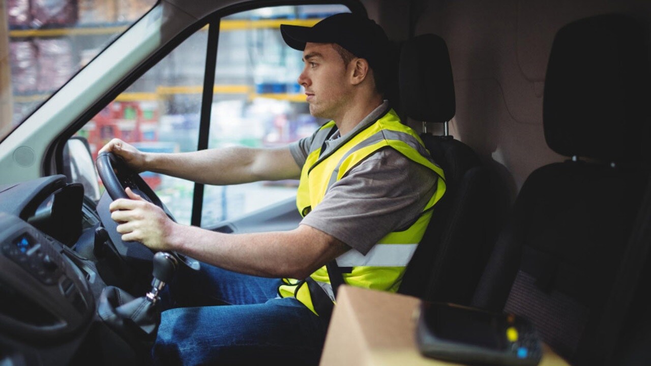 Male driving a delivery van loaded with boxes for international parcel delivery.