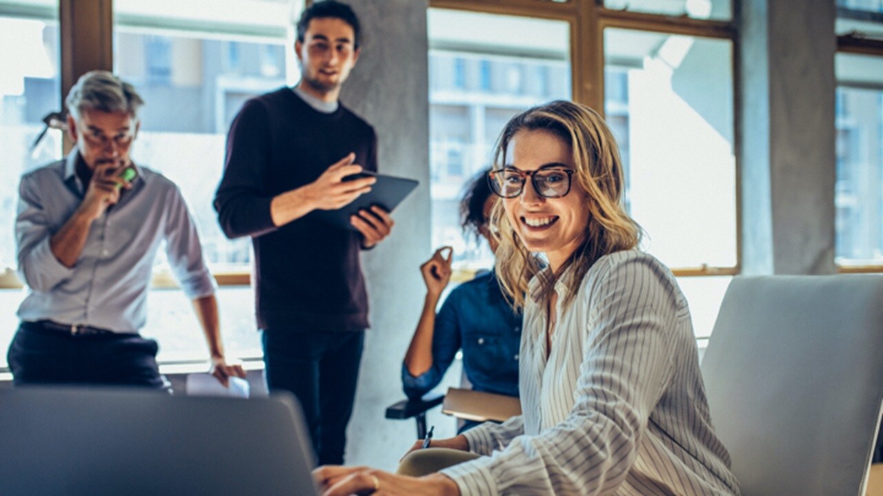 A team of employees looking at SCM dashboard in a laptop in an office.