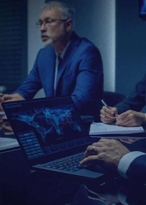 A group of business professionals in a dimly lit conference room, engaged in a serious discussion.