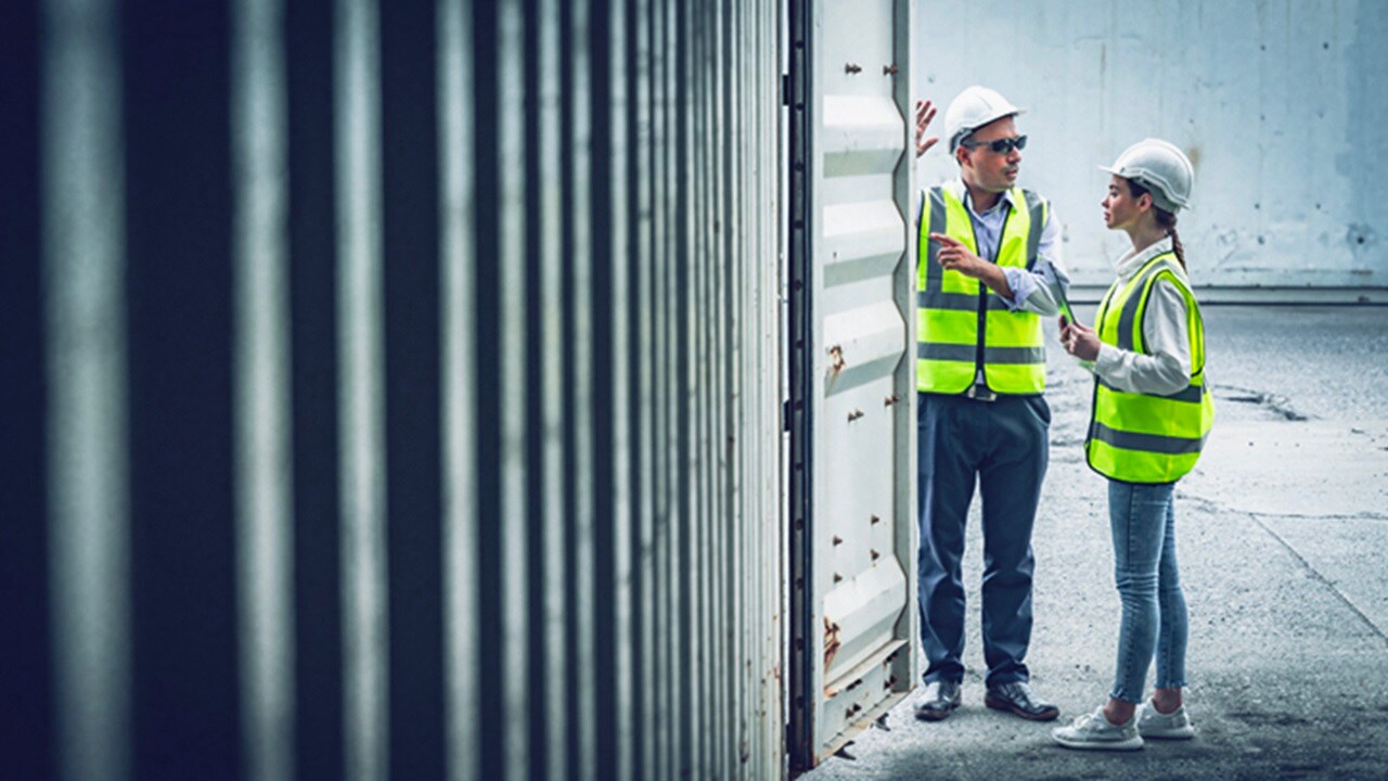 Two workers in protective gear discussing near a cargo container