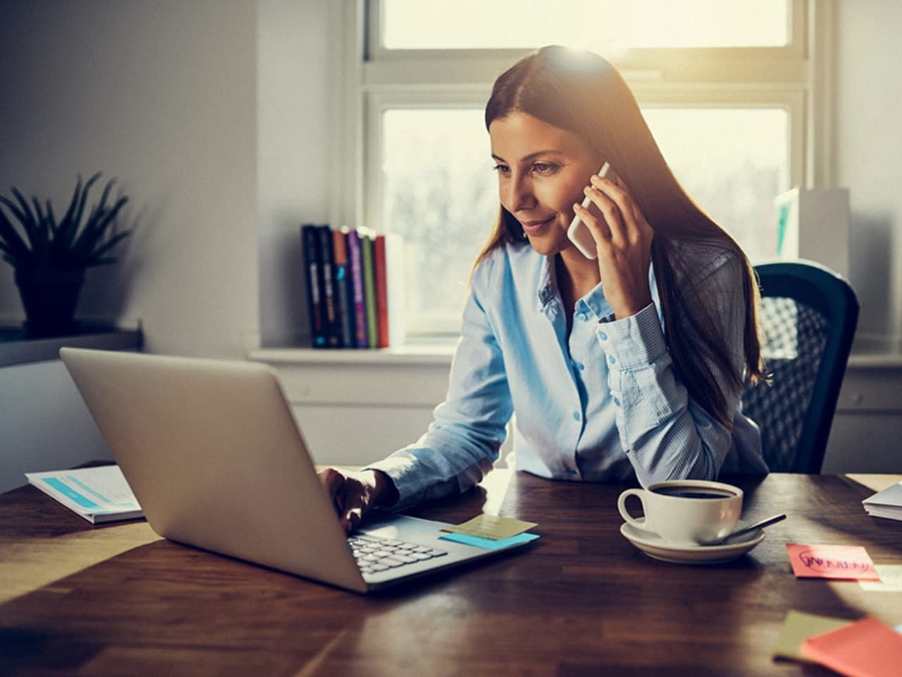 Professional woman working on laptop and talking on phone, representing remote IT support and digital workplace solutions