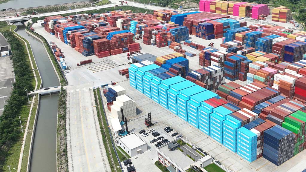 Aerial view of a large intermodal container yard with stacked shipping containers in various colors and brands.